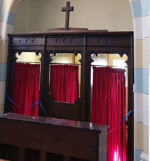 Confessional with red curtains and small cross on top